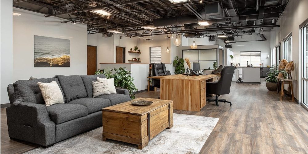 Modern office interior featuring a gray sofa, wooden coffee table, and a workspace with desks and plants, illustrating a tenant improvement by AIS Commercial Construction.