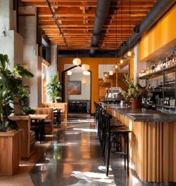 Modern restaurant interior with a wooden bar, stylish seating, and vibrant orange walls, showcasing a blend of natural elements and contemporary design, reflecting AIS Commercial Construction's remodeling expertise.